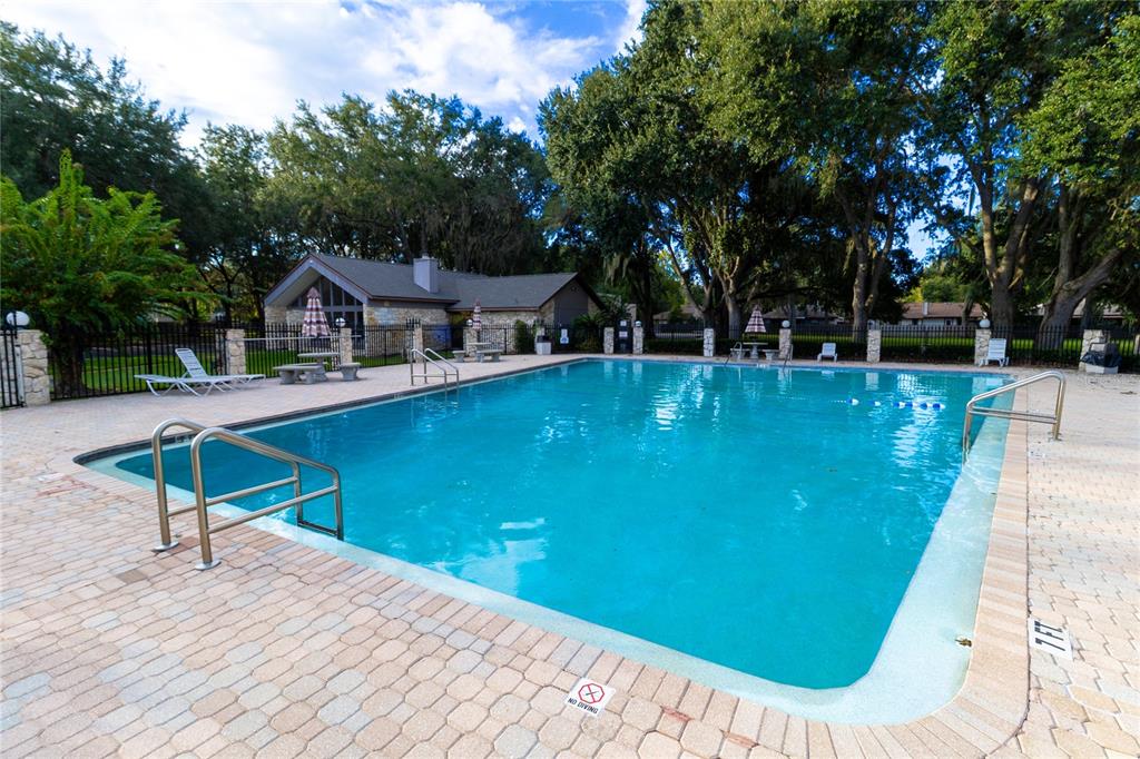 A rectangular outdoor swimming pool is surrounded by a paved deck and mature trees — 3758 NW 56TH LANE, GAINESVILLE, FL