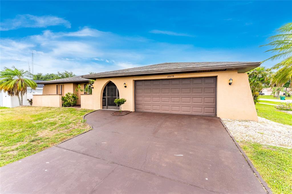 A single-story house with a tan stucco exterior, a brown garage door, and a driveway — 23278 MCNAMEE AVENUE, PORT CHARLOTTE, FL