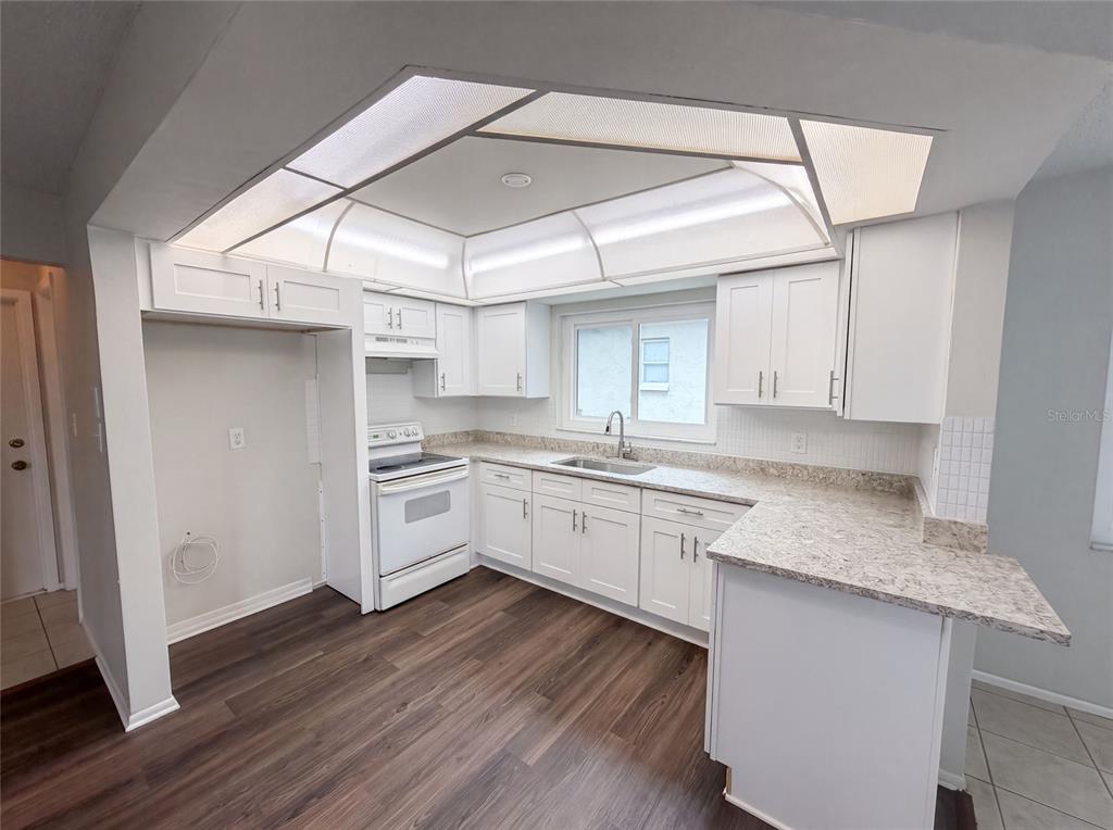 A kitchen with white cabinets, laminate countertops, a white stove, and dark wood-look flooring — 8053 EMBASSY BOULEVARD, PORT RICHEY, FL