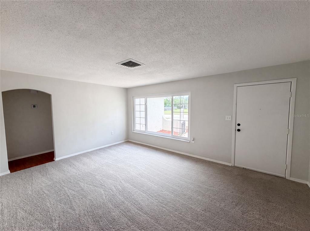 A carpeted living room features a large window, a white door, and an arched entryway — 8053 EMBASSY BOULEVARD, PORT RICHEY, FL