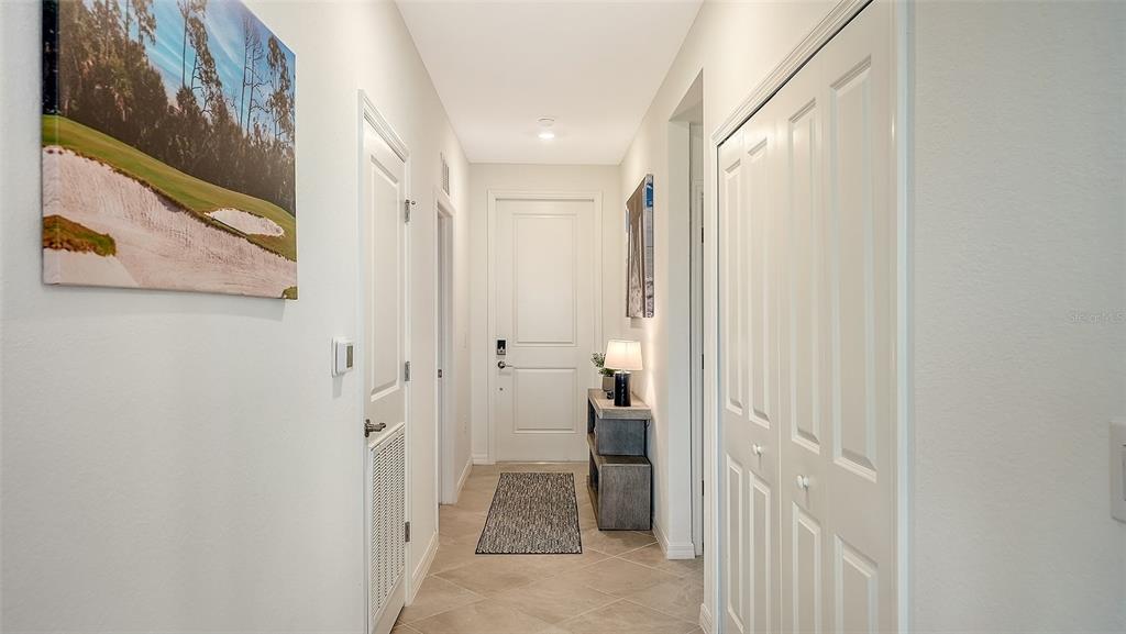 A hallway with tiled floors, white doors, a small console table, and wall art — 12280 WELLEN GOLF STREET UNIT 307, VENICE, FL