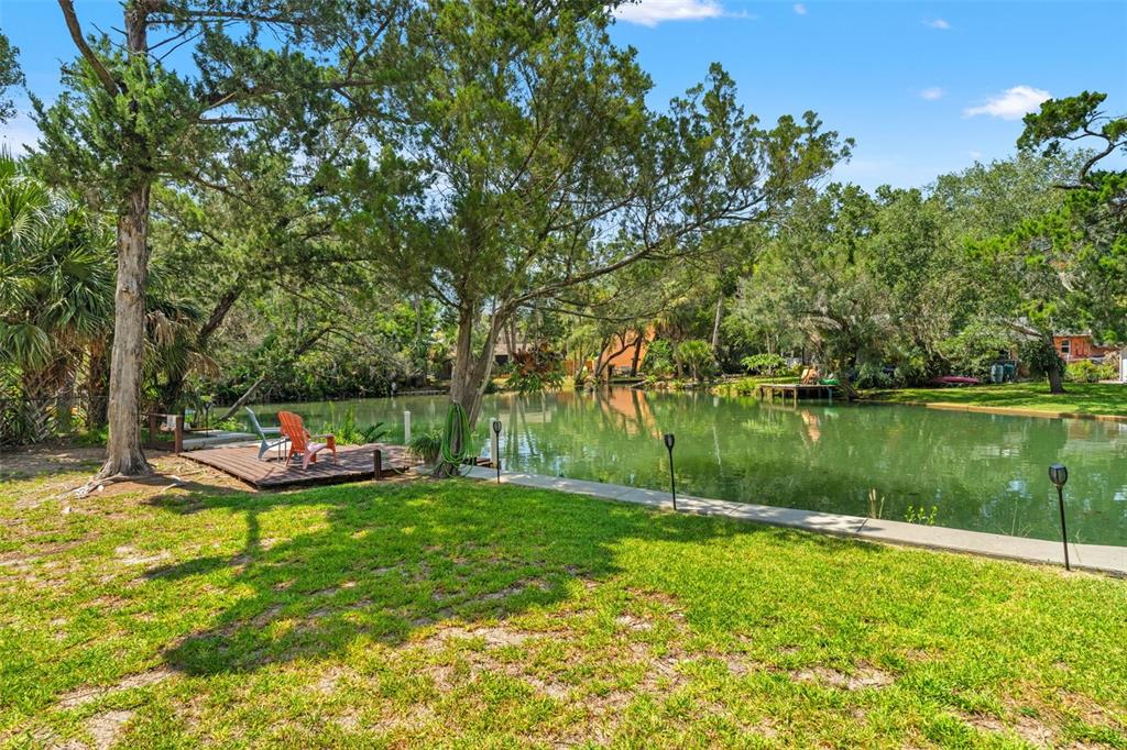 A grassy backyard features a wooden deck with chairs overlooking a calm canal — 6053 PALM CREEK DRIVE, WEEKI WACHEE, FL