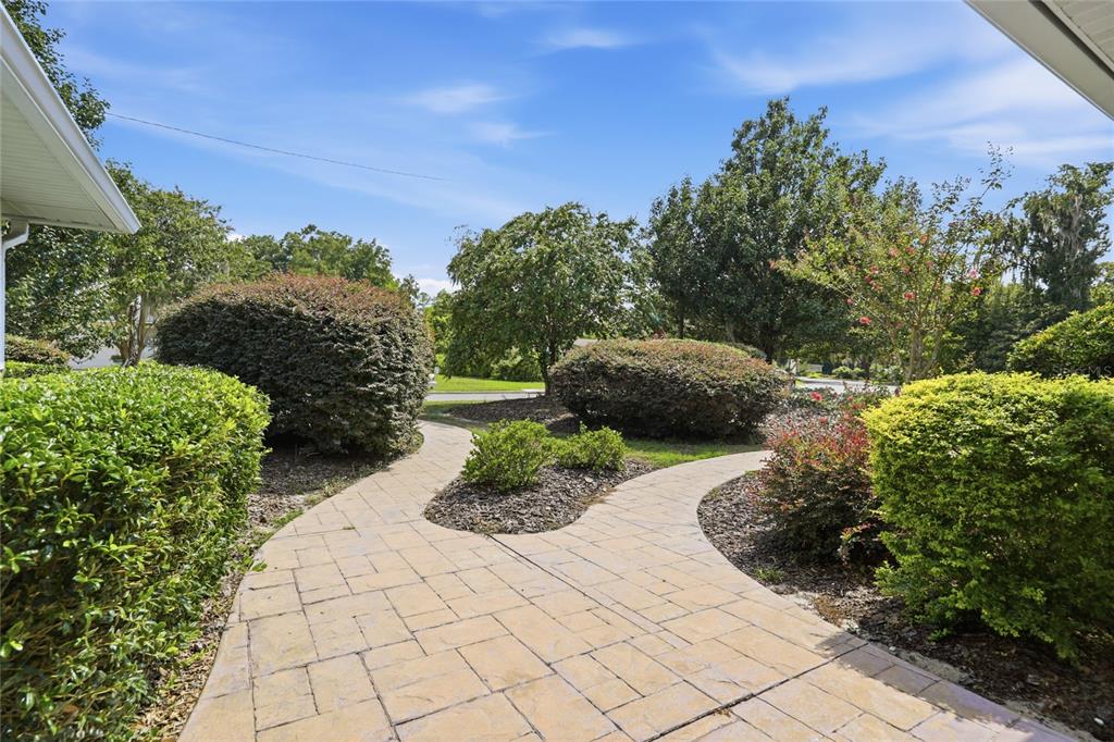 A paved walkway winds through a landscaped front yard with shrubs and mature trees — 2138 NW 30TH PLACE, GAINESVILLE, FL
