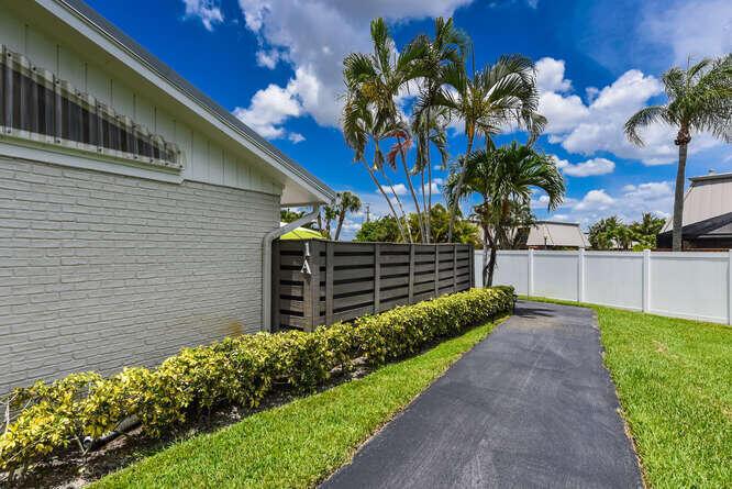 A paved walkway runs alongside a light-colored brick house with a dark wood privacy fence — 1801 S Us Highway 1 # 1a, Jupiter FL 33477, JUPITER, FL