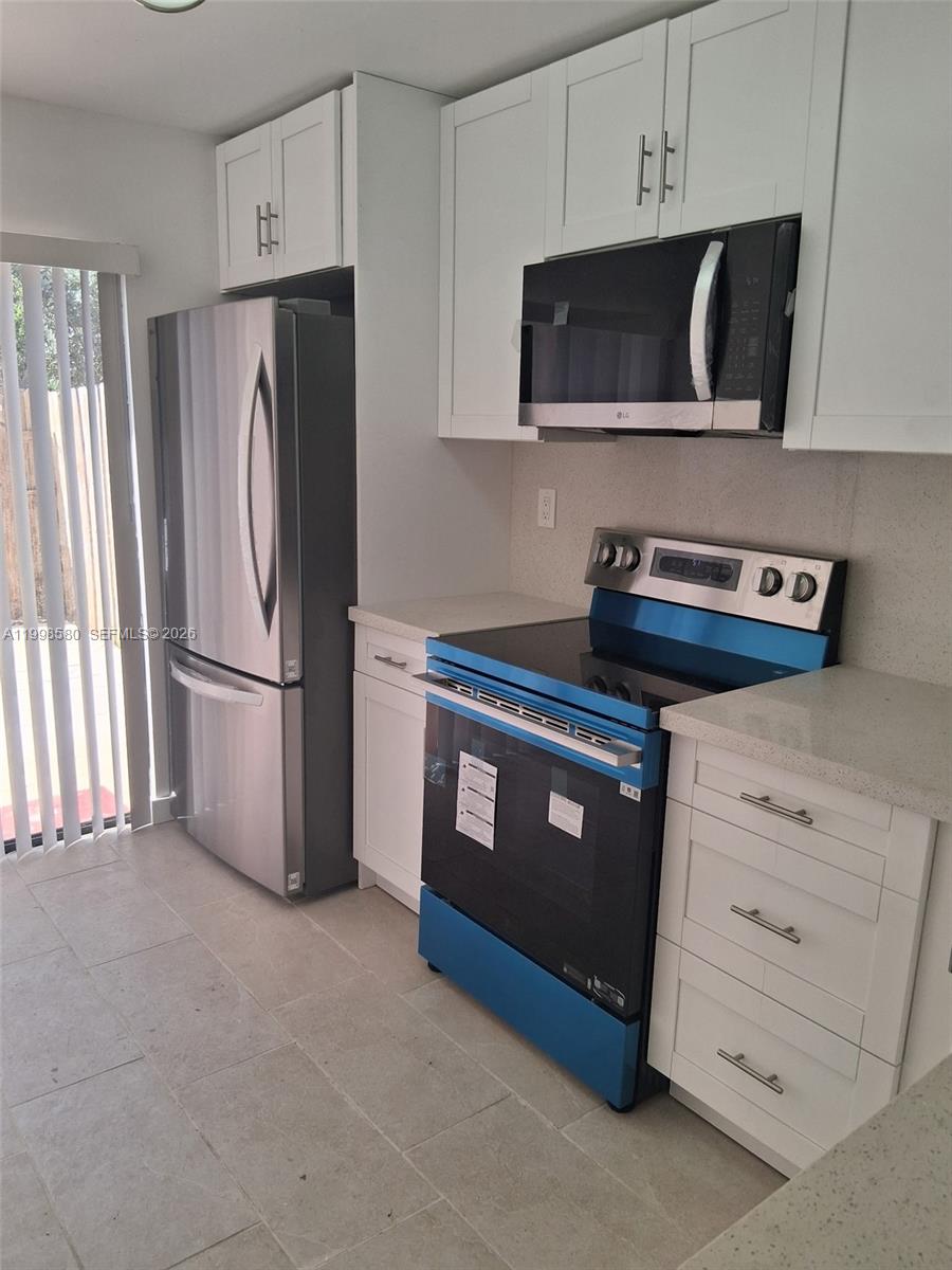 A kitchen features white cabinets, stainless steel appliances, and light-colored tile flooring — 10029 SW 77th Ct # 0, Miami FL 33156, MIAMI, FL
