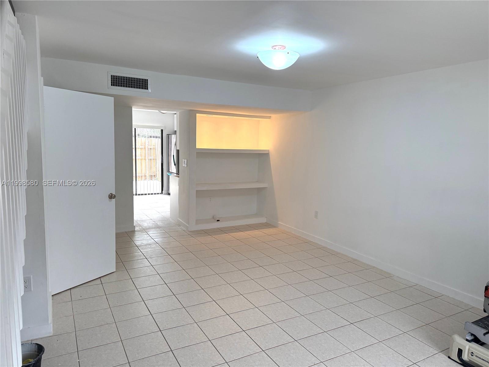A room with white walls, tile flooring, a built-in shelf, and an open doorway — 10029 SW 77th Ct # 0, Miami FL 33156, MIAMI, FL