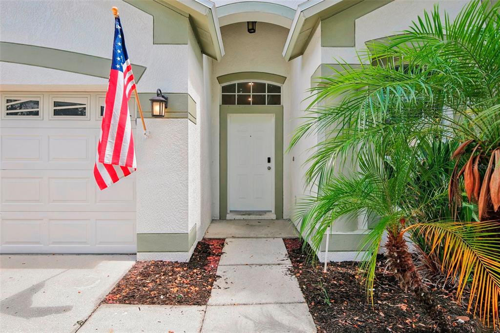 A white front door with a transom window sits beside a garage and palm tree — 10616 LITTLE BEND LANE, RIVERVIEW, FL