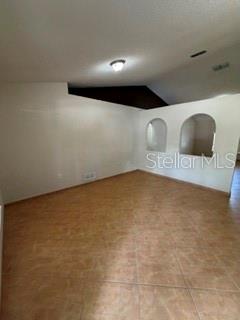 An empty room with tan tile flooring, white walls, and two arched wall niches — 527 KILIMANJARO DRIVE, KISSIMMEE, FL