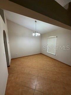 An empty room with tan tile flooring, a vaulted ceiling, and a hanging light fixture — 527 KILIMANJARO DRIVE, KISSIMMEE, FL