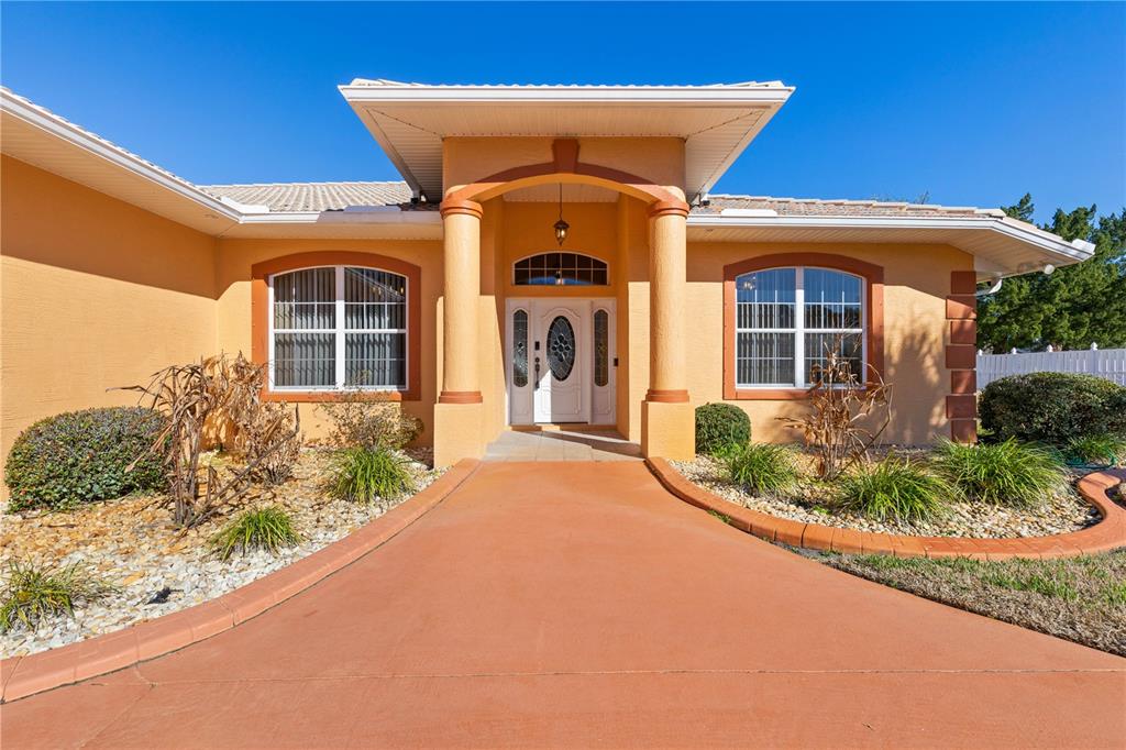 The exterior of a peach-colored house features a covered entryway with columns and a walkway — 34 WOODFIELD DRIVE, PALM COAST, FL