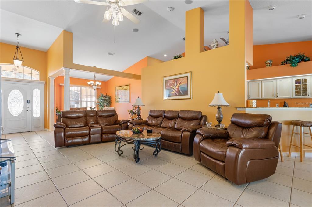 A living room with tile floors, brown leather furniture, and orange walls under a vaulted ceiling — 34 WOODFIELD DRIVE, PALM COAST, FL