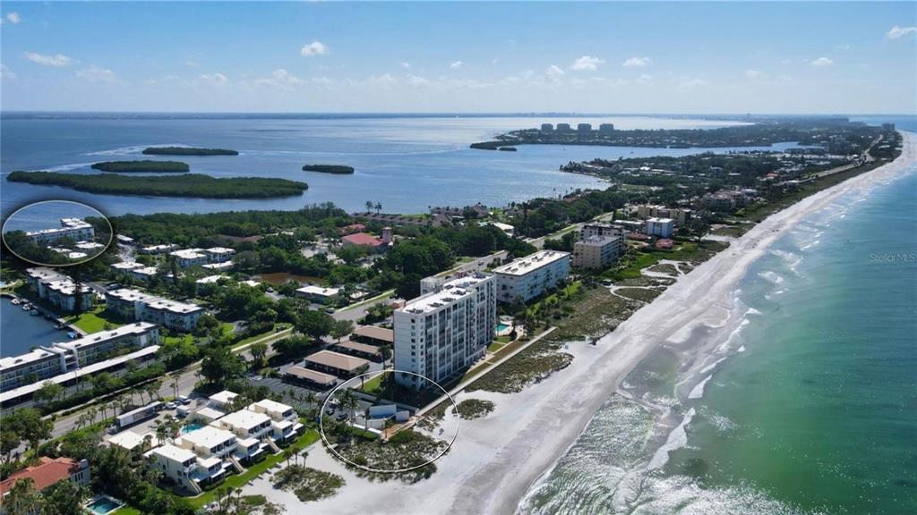 An aerial view shows beachfront condominiums, a sandy shoreline, and surrounding coastal vegetation — 600 SUTTON PLACE UNIT B302, LONGBOAT KEY, FL