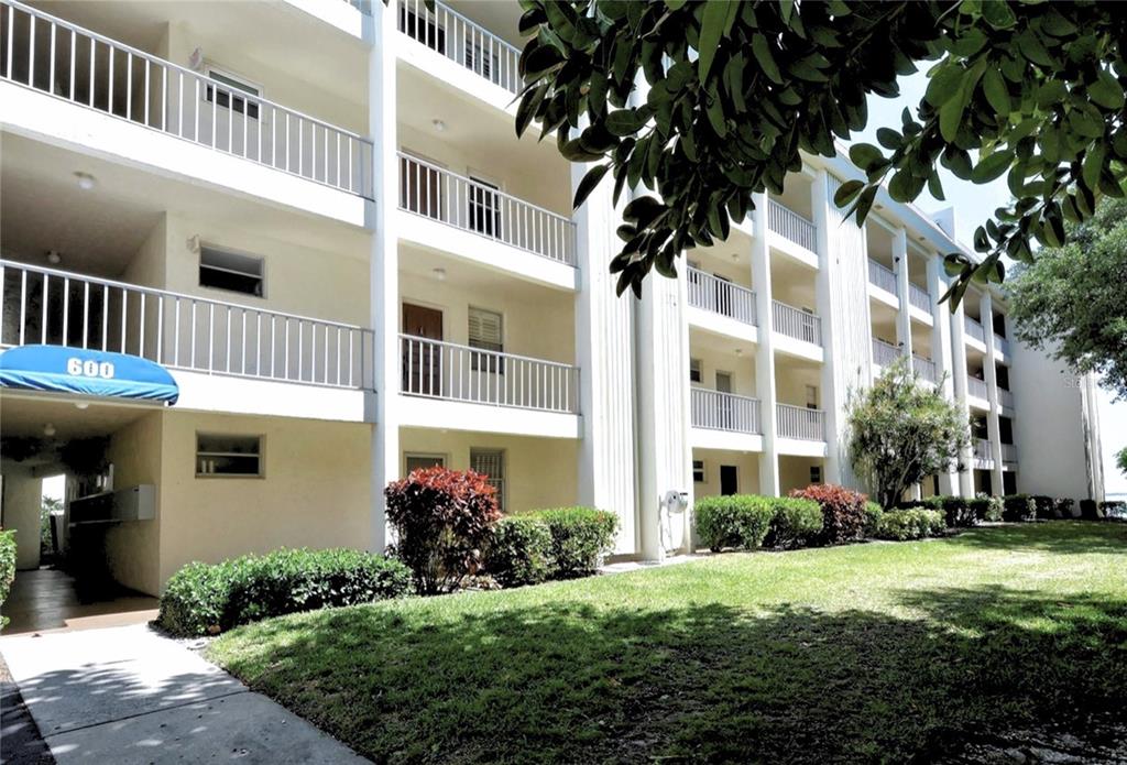 A multi-story apartment building with white balconies and a blue awning over the entrance — 600 SUTTON PLACE UNIT B302, LONGBOAT KEY, FL