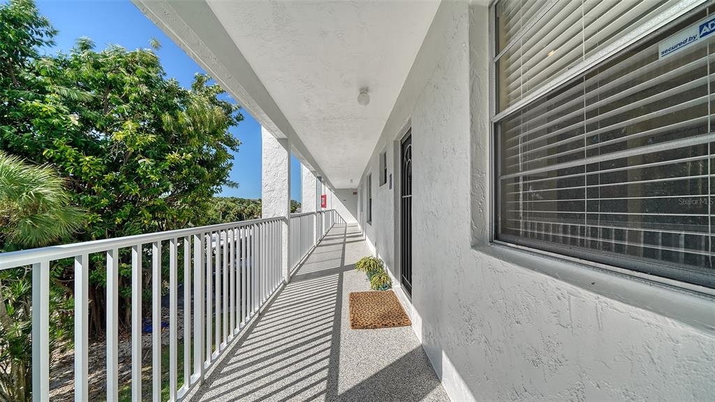 An outdoor balcony features a white railing, a textured floor, and a door with a window — 600 SUTTON PLACE UNIT B302, LONGBOAT KEY, FL