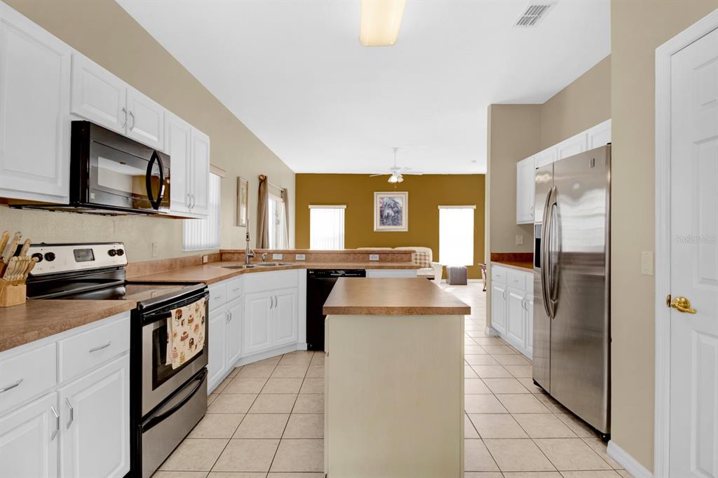 A kitchen with white cabinets, stainless steel appliances, a central island, and tan tile flooring — 4603 CUMBRIAN LAKES DRIVE, KISSIMMEE, FL