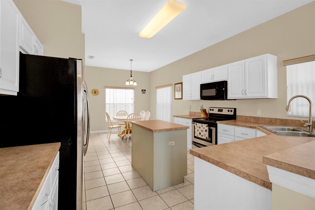 A kitchen with white cabinets, tan countertops, a center island, and an adjacent dining area — 4603 CUMBRIAN LAKES DRIVE, KISSIMMEE, FL