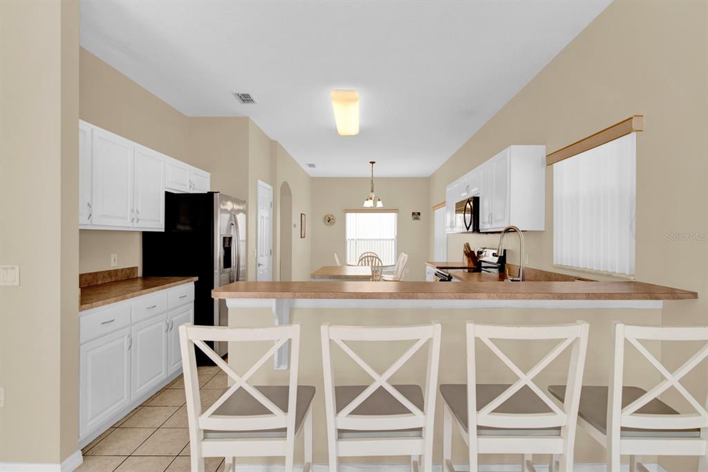 A kitchen with white cabinets, a breakfast bar with four chairs, and tile flooring — 4603 CUMBRIAN LAKES DRIVE, KISSIMMEE, FL