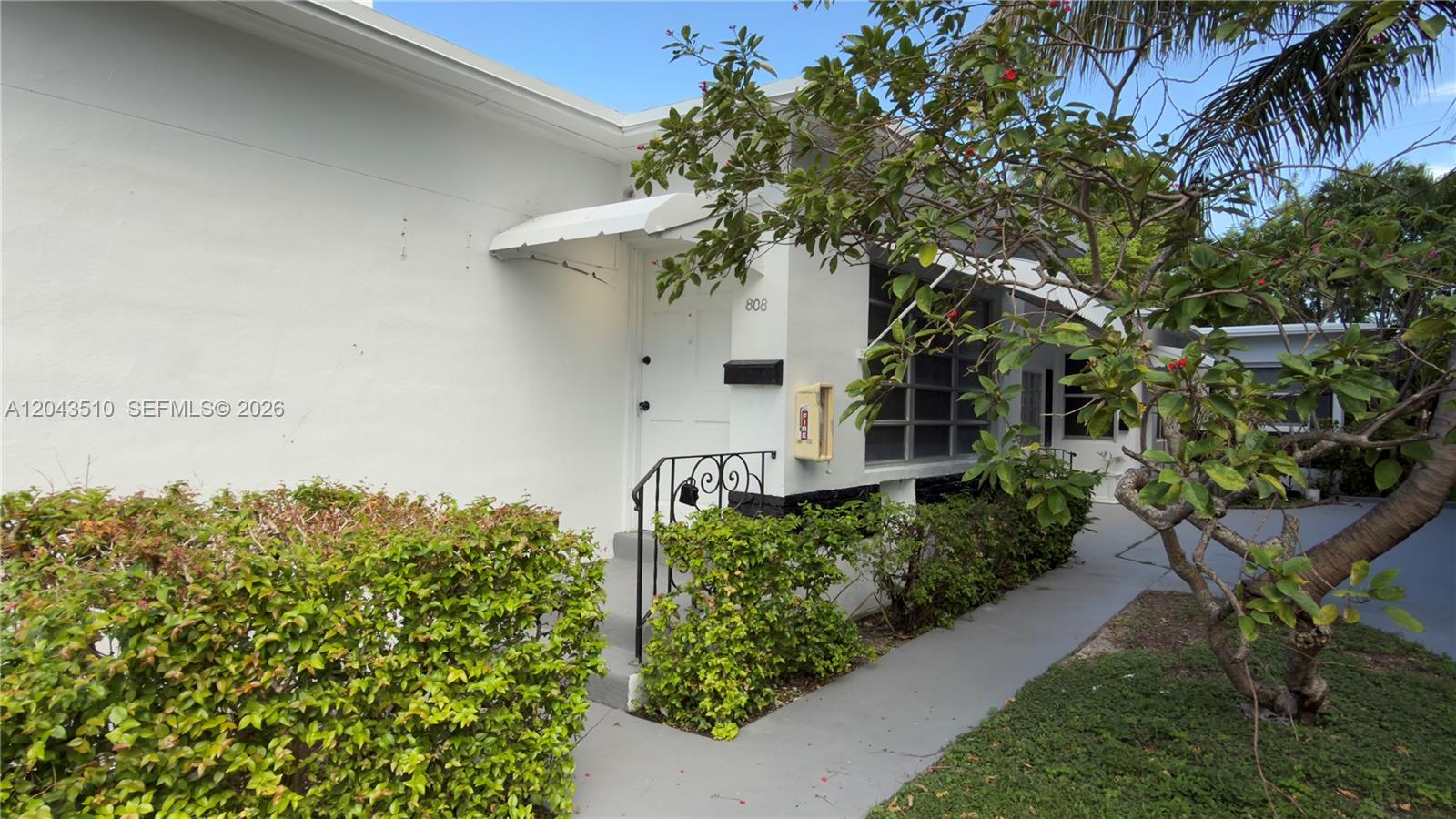A white building exterior features a front door, a small metal railing, and landscaping — 808 84th St # 808, Miami Beach FL 33141, MIAMI BEACH, FL