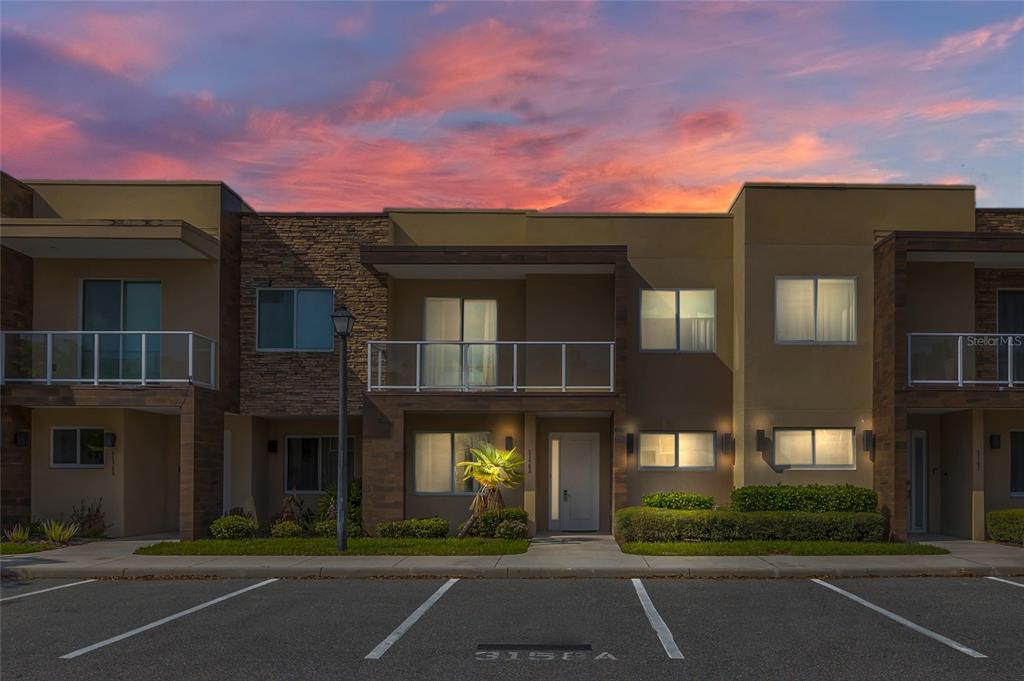 A two-story townhouse exterior with a balcony, stone accents, and a parking space at dusk — 3158 BRASILIA AVENUE, KISSIMMEE, FL
