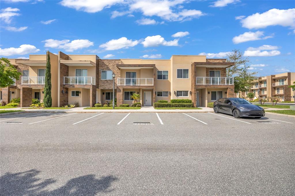 A modern multi-story townhouse complex features tan stucco walls, stone accents, and private balconies — 3158 BRASILIA AVENUE, KISSIMMEE, FL