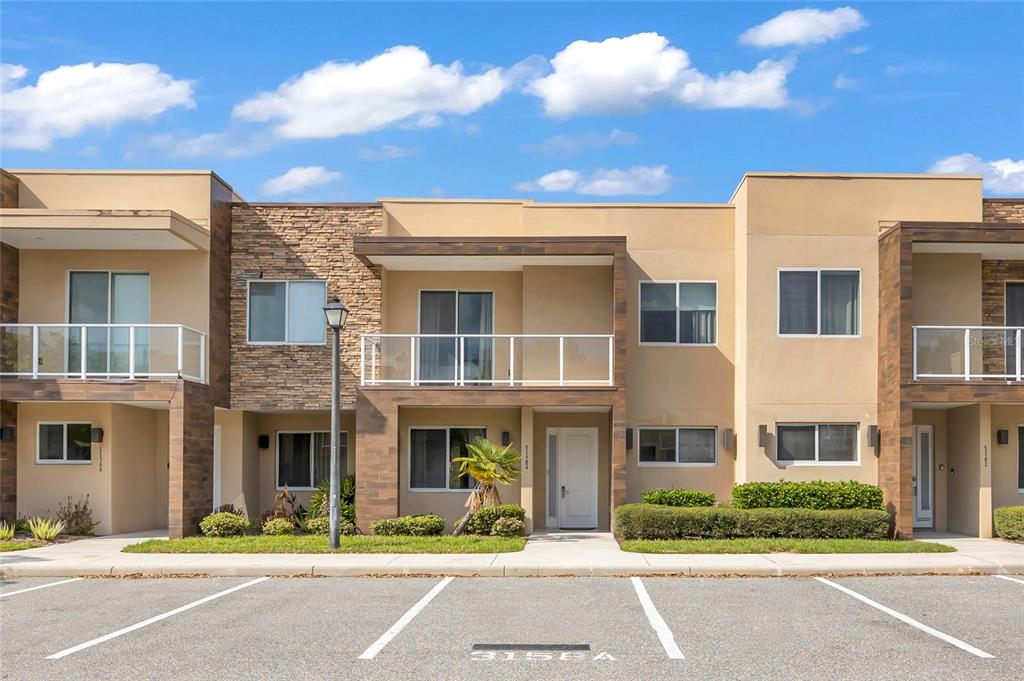A two-story townhouse exterior features tan stucco, stone accents, and private balconies with glass railings — 3158 BRASILIA AVENUE, KISSIMMEE, FL