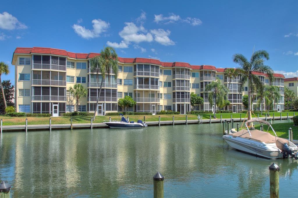 A multi-story apartment building with screened balconies sits along a canal with docked boats — 1250 N PORTOFINO DRIVE UNIT 107MAR, SARASOTA, FL