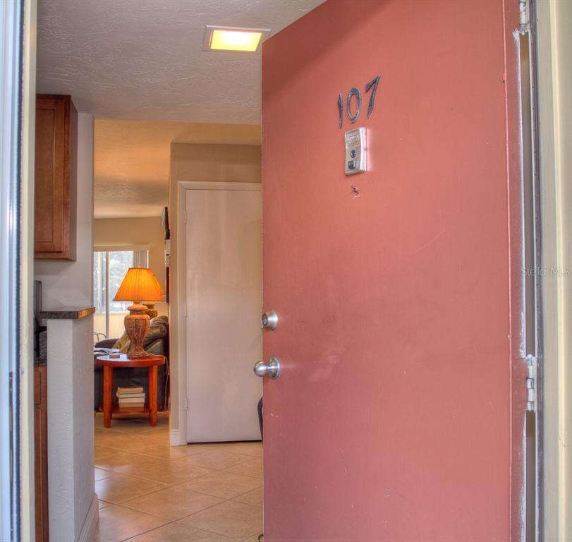 An open door reveals a tiled entryway leading to a living area with a table lamp — 1250 N PORTOFINO DRIVE UNIT 107MAR, SARASOTA, FL