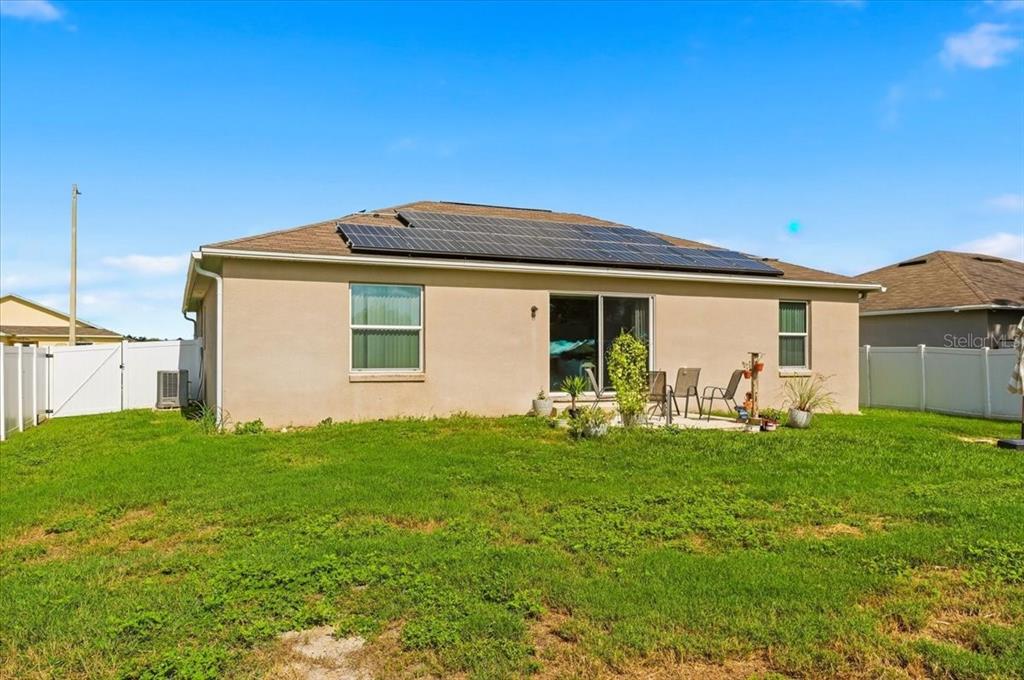 The back exterior of a tan house features a patio, solar panels, and a fenced yard — 180 SOLIS DRIVE, WINTER HAVEN, FL