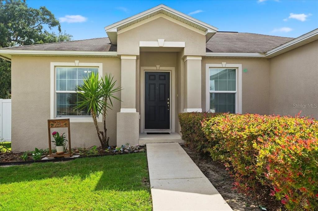 A tan single-story house features a dark front door, a concrete walkway, and landscaping — 180 SOLIS DRIVE, WINTER HAVEN, FL