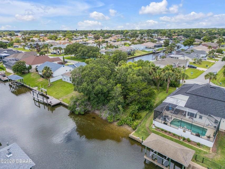 An aerial view shows a vacant, tree-covered waterfront lot between two residential houses — 9 N CHRISTOPHER COURT, PALM COAST, FL