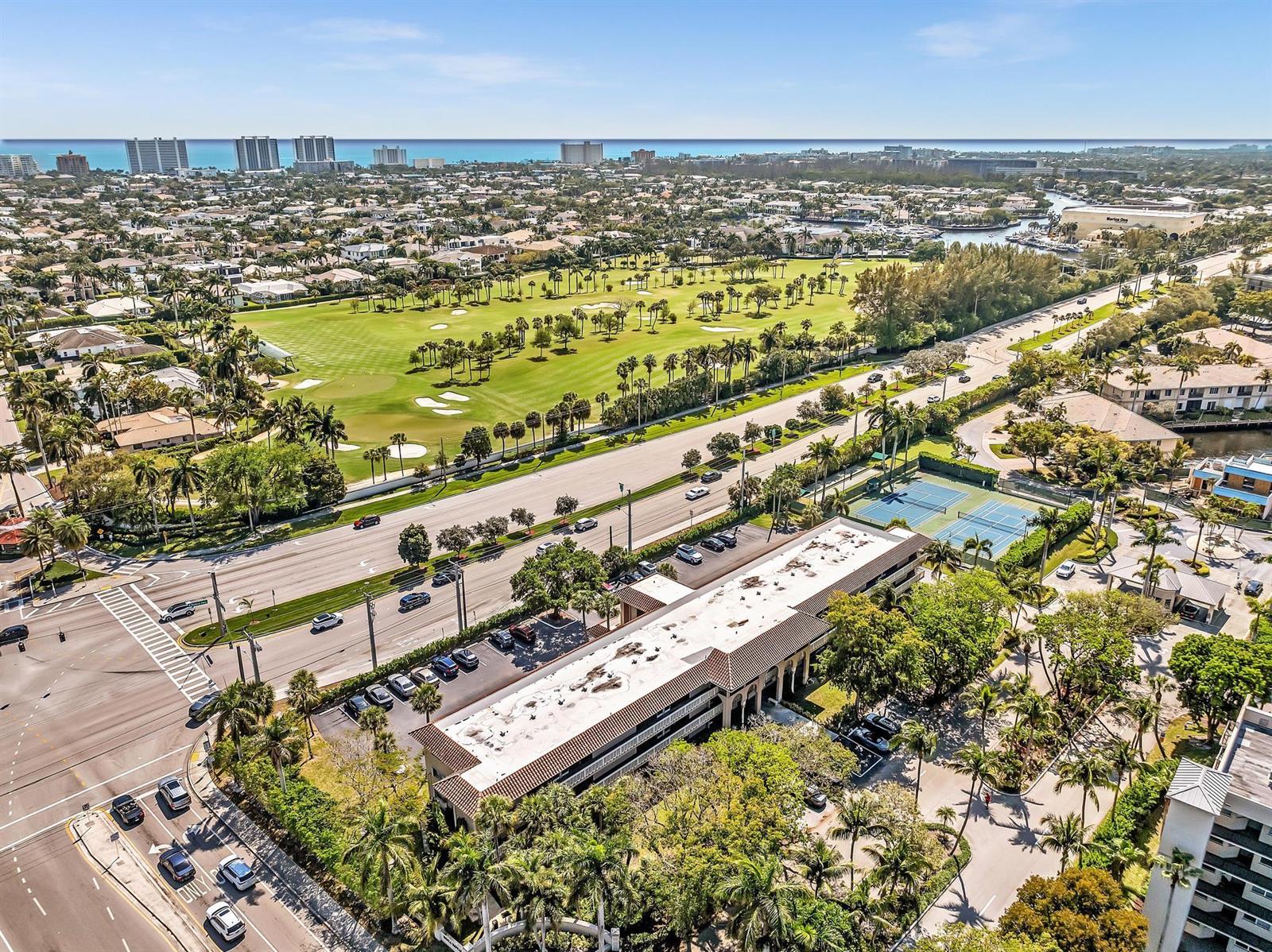 An aerial view shows a multi-story building, tennis courts, a golf course, and nearby oceanfront — 100 Royal Palm Way # 303, Boca Raton FL 33432, BOCA RATON, FL