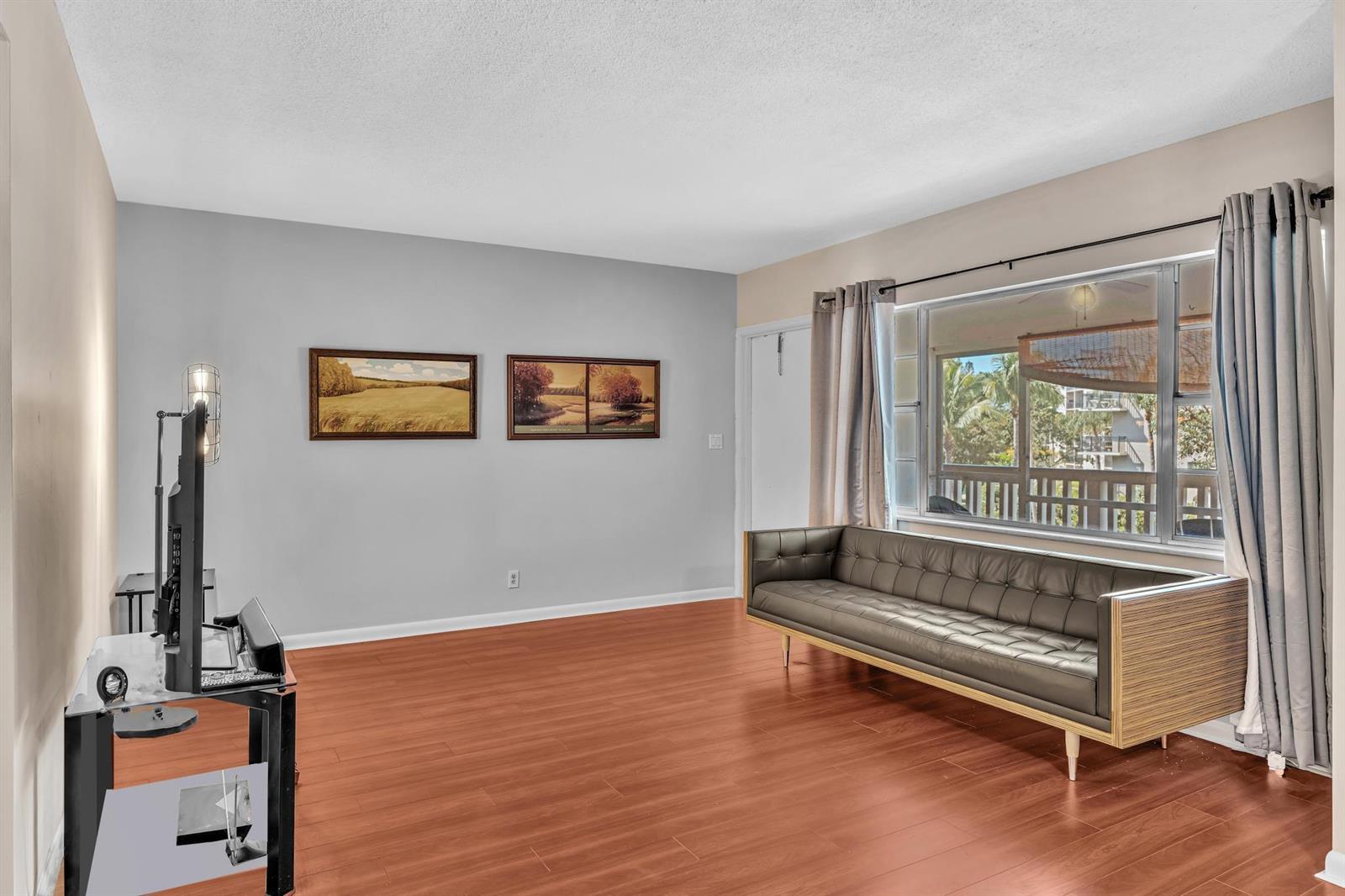A living room features wood-look flooring, a grey sofa, a television stand, and two framed paintings — 100 Royal Palm Way # 303, Boca Raton FL 33432, BOCA RATON, FL