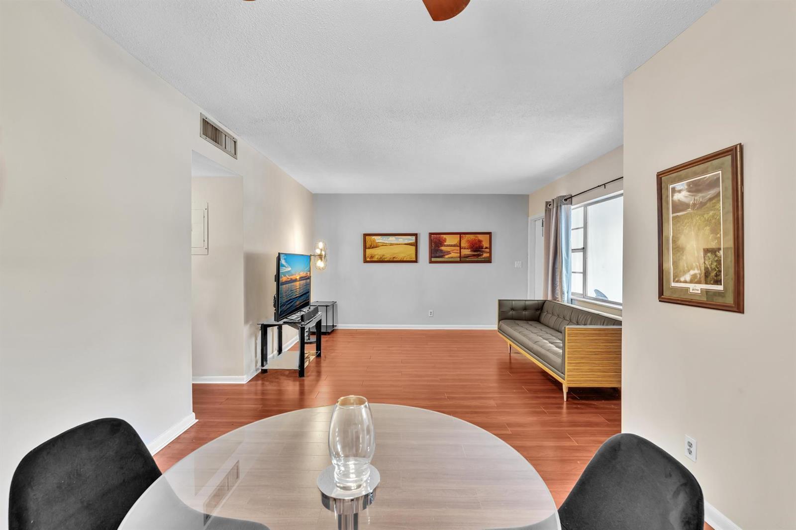A living room with wood flooring, a grey sofa, a television, and a dining table — 100 Royal Palm Way # 303, Boca Raton FL 33432, BOCA RATON, FL