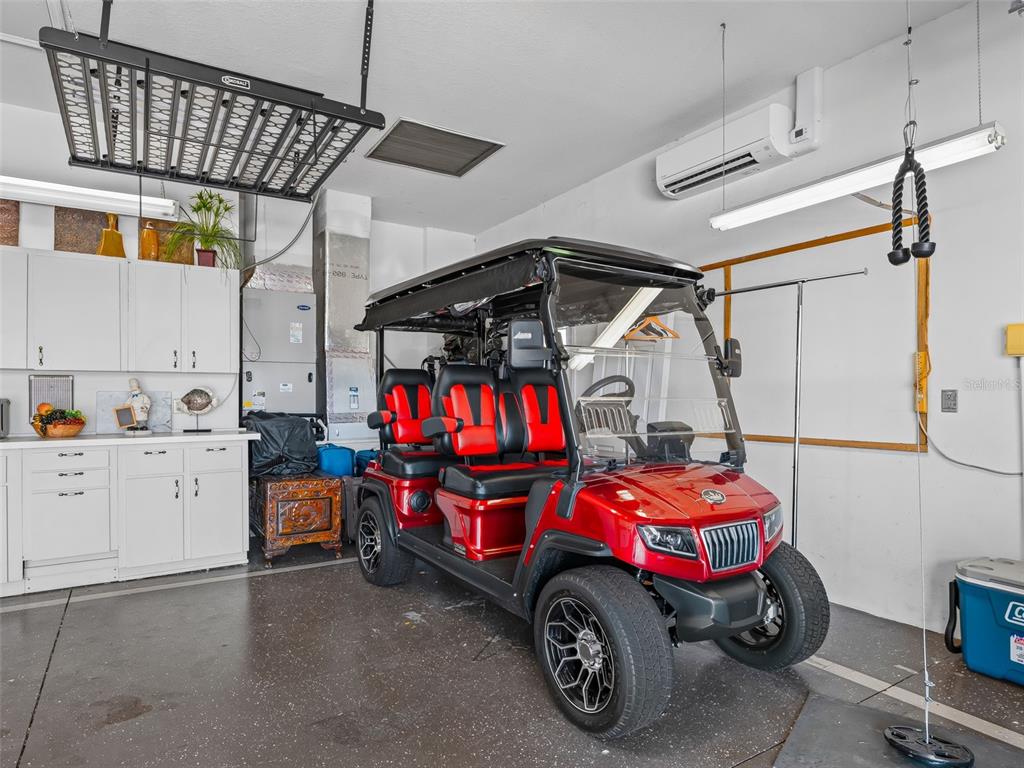 A red golf cart is parked inside a garage with white cabinets and a mini-split unit — 11768 SE 176TH PLACE ROAD, SUMMERFIELD, FL