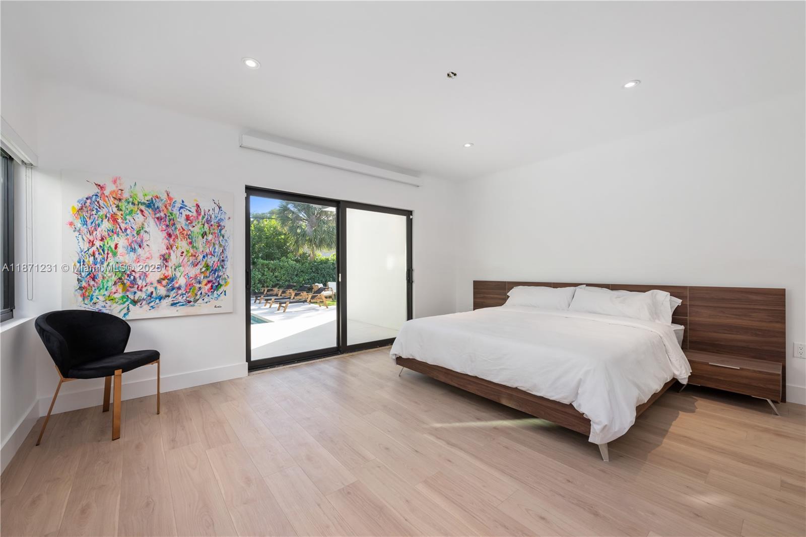 A modern bedroom features a wood-frame bed, a black accent chair, and sliding glass doors — 900 W 47th Ct, Miami Beach FL 33140, MIAMI BEACH, FL