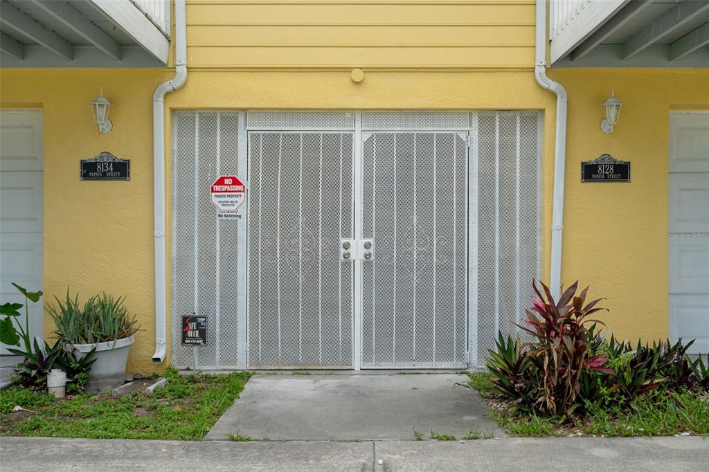 A yellow building exterior features a central gated entrance flanked by two address plaques — 8128 PAPAYA STREET, PORT RICHEY, FL