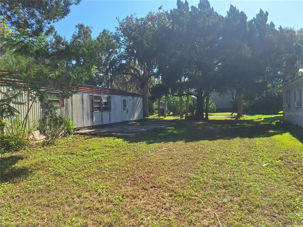 A mobile home sits next to a grassy yard with large trees and a concrete patio — 6501 WERNER AVENUE, NEW PORT RICHEY, FL