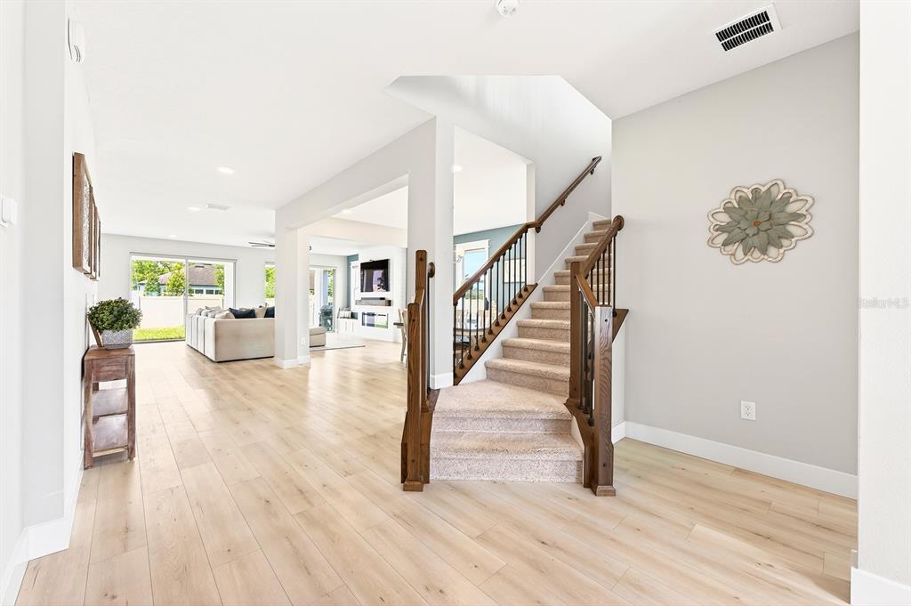 A bright entryway features light wood flooring, a carpeted staircase with wood railings, and open-concept living — 2234 MAROON FLAME COURT, OVIEDO, FL