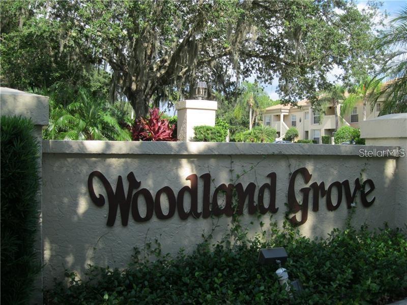 A beige stucco wall displays the Woodland Grove sign in front of trees and apartments — 4397 LONGMEADOW UNIT 35, SARASOTA, FL