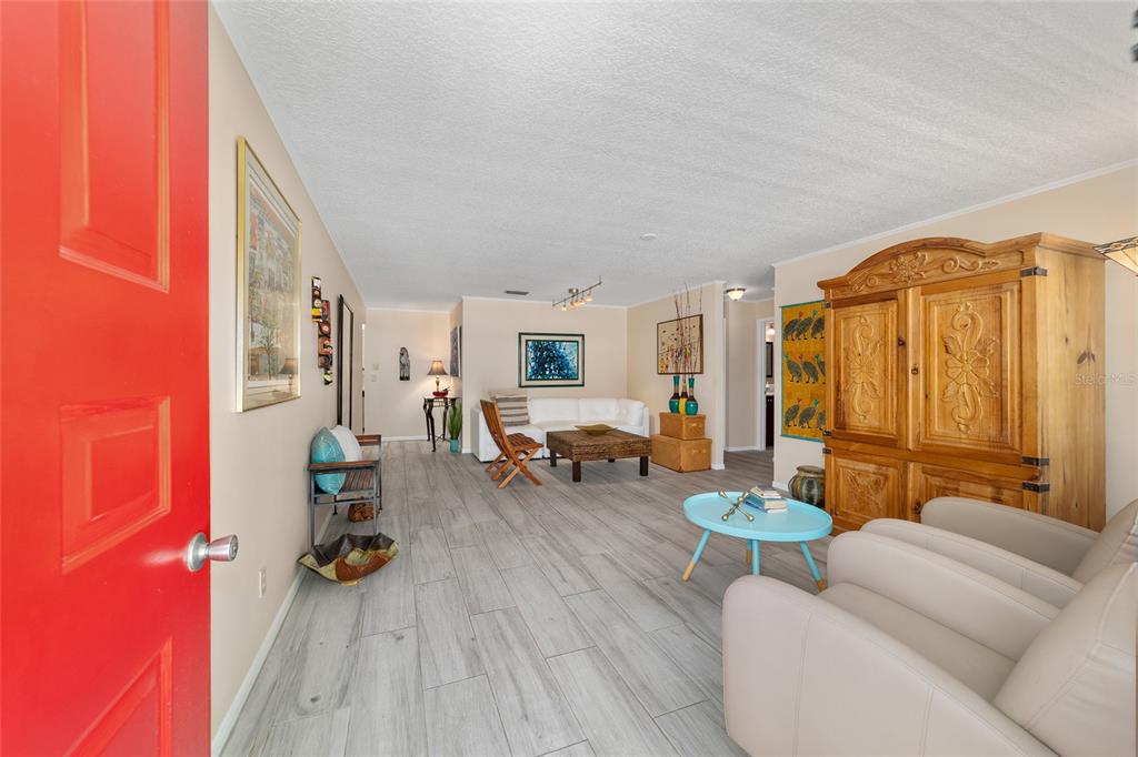 A living room features light wood-look tile flooring, a red door, and a large wooden armoire — 8625 SW 94 LANE UNIT G, OCALA, FL