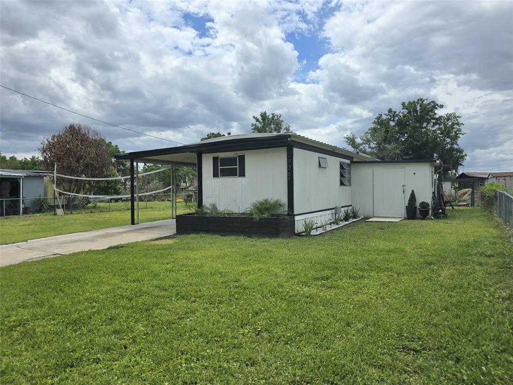 A single-story mobile home with a carport and a black planter box in the front yard — 2936 N PALM CIRCLE, HAINES CITY, FL