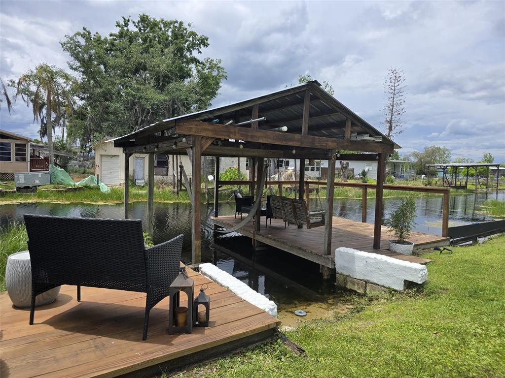 A wooden boat dock with a covered seating area sits over a canal near a lawn — 2936 N PALM CIRCLE, HAINES CITY, FL