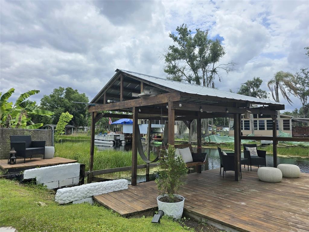 A wooden deck with a covered pavilion overlooks a canal with a boat and seating — 2936 N PALM CIRCLE, HAINES CITY, FL