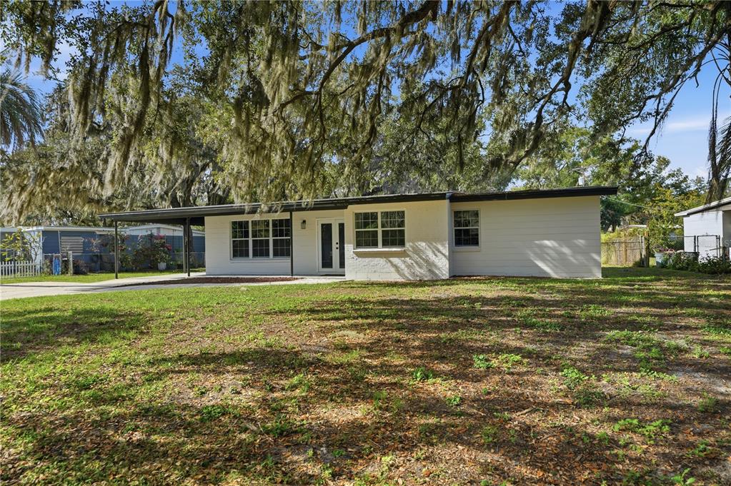A single-story white house with a flat roof and a covered carport under large trees — 707 ABERDEEN CIRCLE, TAMPA, FL