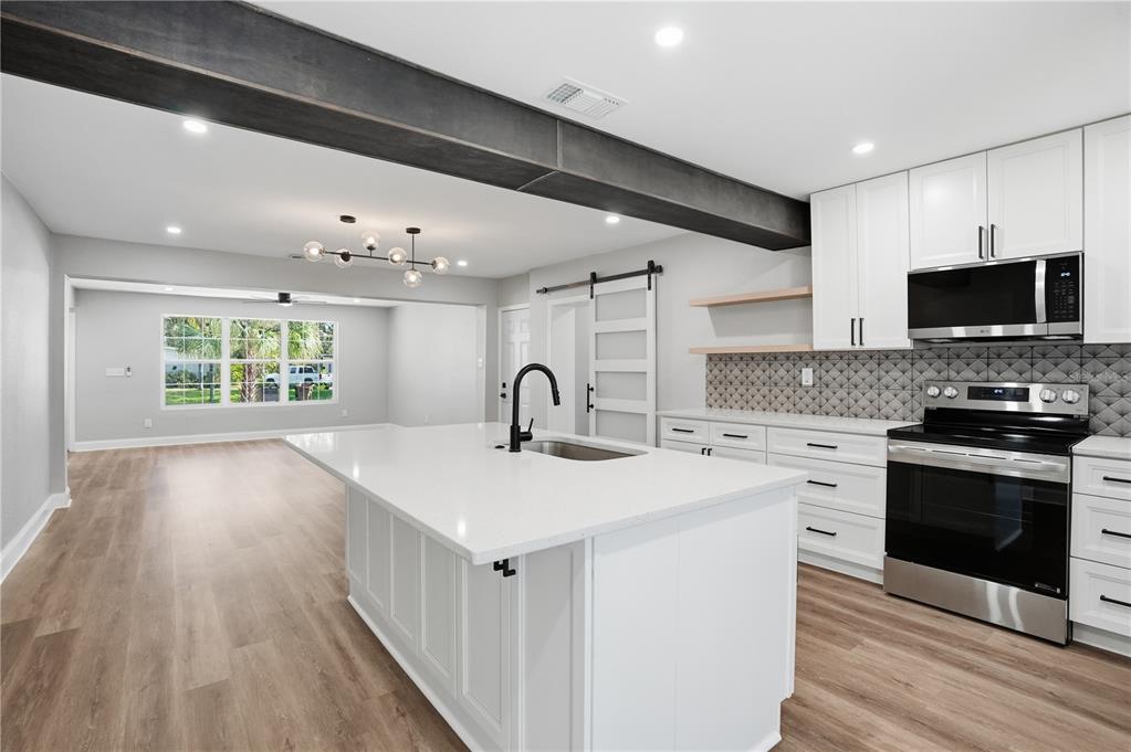 A modern kitchen features white cabinetry, a large center island, and a dark structural beam — 707 ABERDEEN CIRCLE, TAMPA, FL