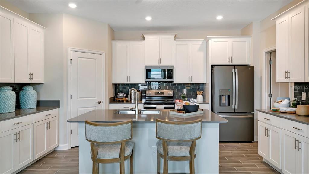 A modern kitchen features white cabinetry, a gray island with seating, and stainless steel appliances — 5626 FIONA LANE, ST CLOUD, FL