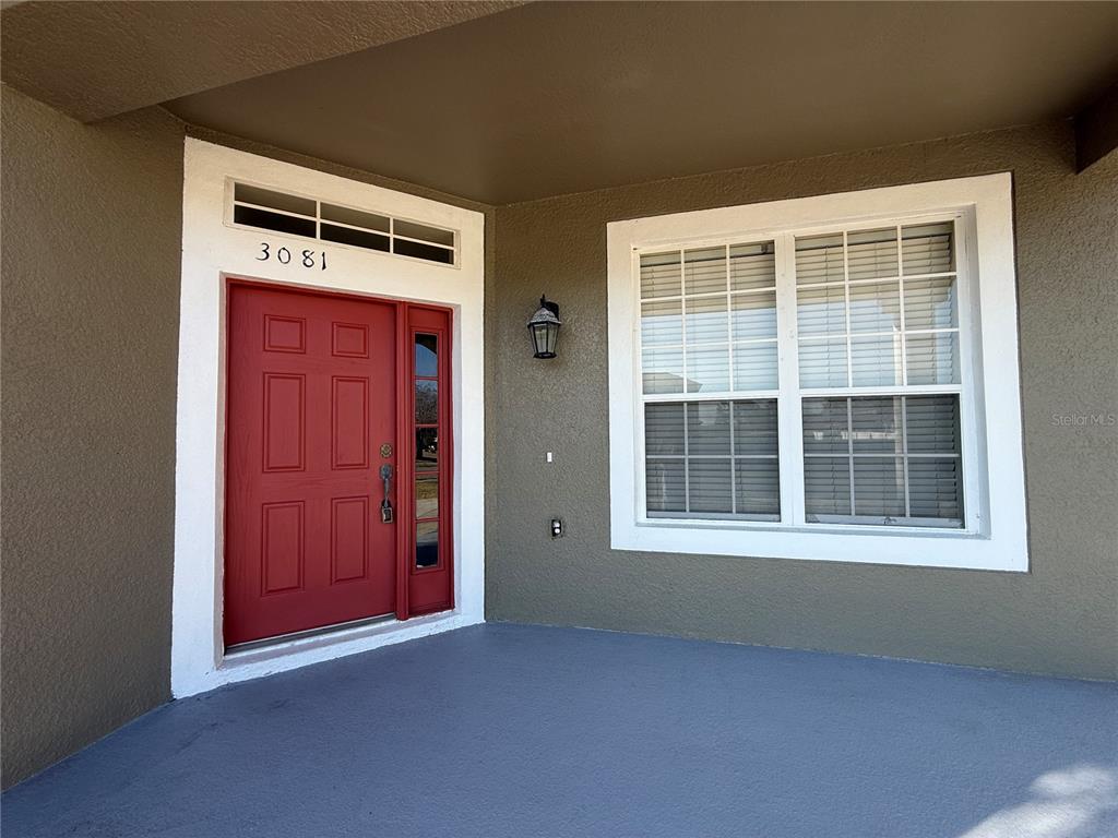 A red front door with a side window and house number sits on a porch — 3081 MARSHFIELD PRESERVE WAY, KISSIMMEE, FL