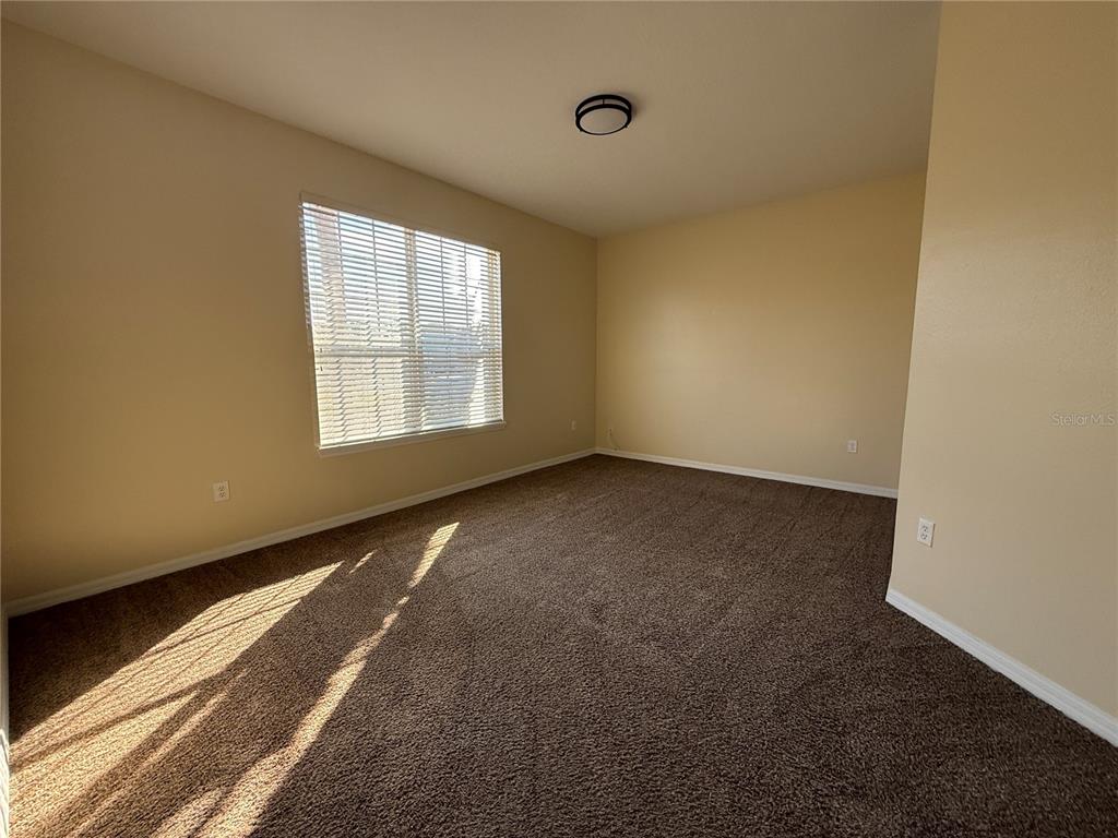 An empty bedroom features beige walls, brown carpeting, and a window with white blinds — 3081 MARSHFIELD PRESERVE WAY, KISSIMMEE, FL
