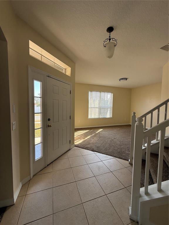 An entryway with tile flooring leads to a carpeted living area with a staircase — 3081 MARSHFIELD PRESERVE WAY, KISSIMMEE, FL