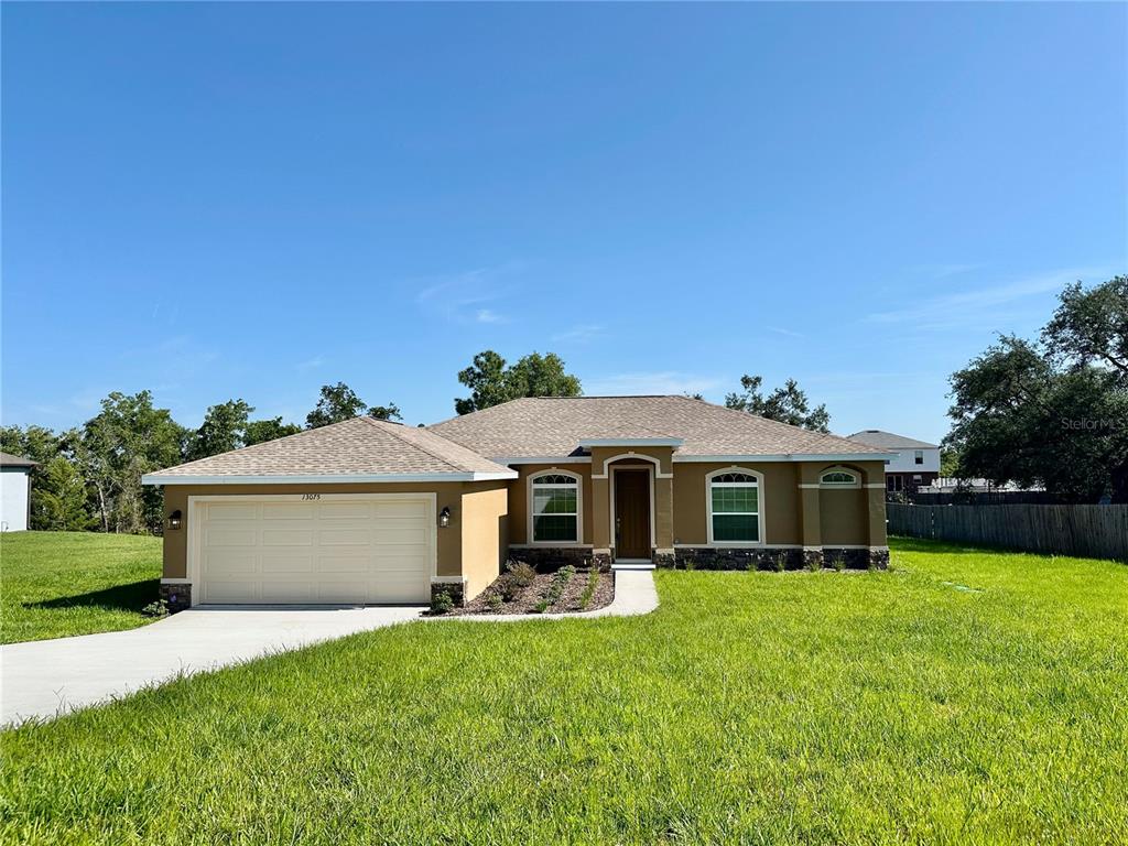 A single-story house with a tan stucco exterior, a two-car garage, and a front walkway — 13075 HOUSE FINCH ROAD, WEEKI WACHEE, FL